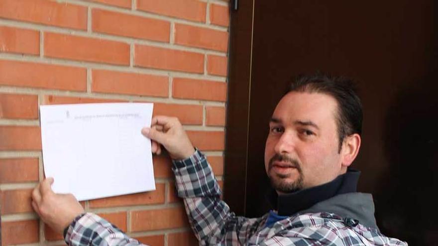 Javier Menéndez coloca una hoja de inscripciones en un portal de El Berrón.