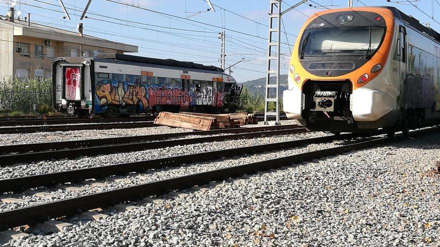 Un tren circula per davant del vagó que espera el seu desballestament, aturat a la platja de vies de l&#039;estació de Sant Vicenç