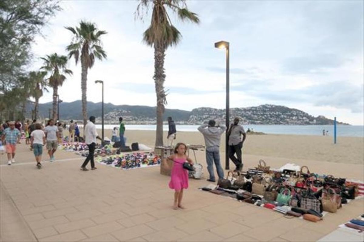 Una niña pasa ante una manta con bolsos falsificados de varias marcas, en Roses.
