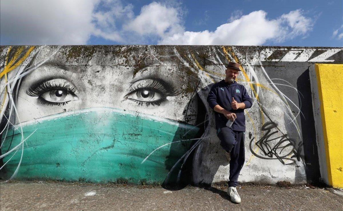 El grafitero belga CAZ posa junto a una de las obras que ha llevado a cabo para dar apoyo al personal médico que lucha contra el coronavirus. La imagen está en la ciudad de Wetteren, Bélgica.