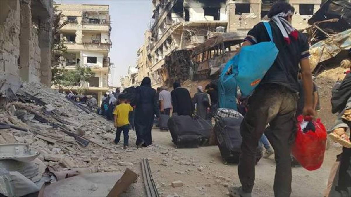 Columnas de gente con algunas pertenencias abandonan Daraya, ayer.