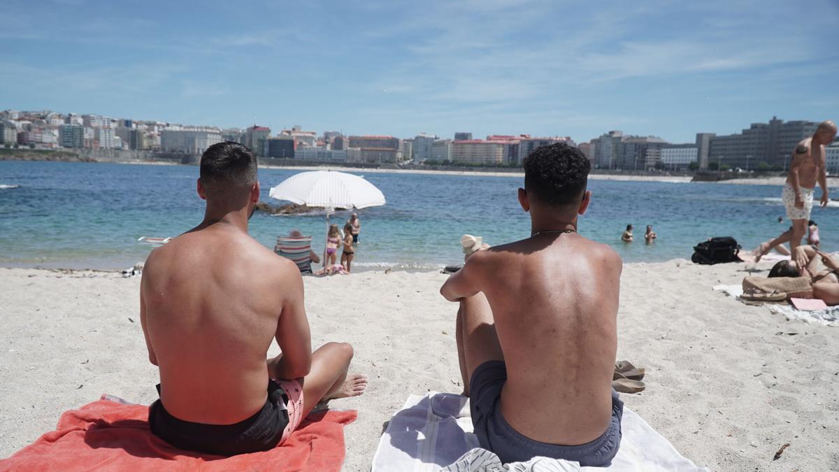 Dos jóvenes sentados al sol, este viernes, en la playa de Riazor, en A Coruña.