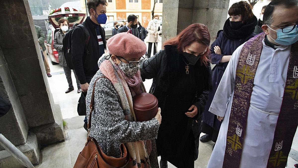 Pino Mesa abraza la urna con las cenizas de Marian Suárez acompañada de su hermana Olga y con el párroco David Cuenca abriendo paso, ayer, antes del funeral de la poeta.