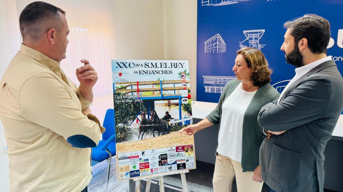 Lola Sánchez, presidenta de la asociación organizadora, explica los detalles del cartel a Martínez y Ballonas.