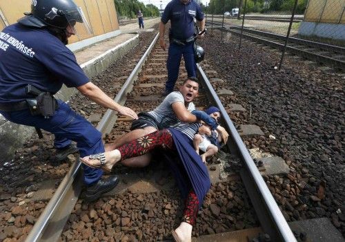Hungarian policemen stand by the family of migrants as they wanted to run away at the railway station in the town of Bicske