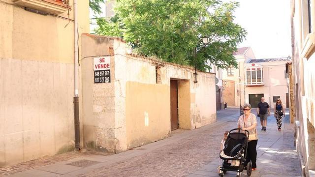 Personas caminan por una de las calles del casco antiguo, junto a un cartel de «se vende».