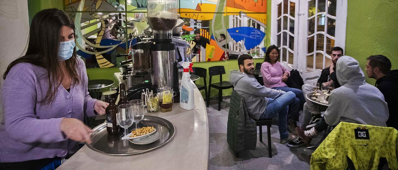 Teresa atiende a uno de los grupos que acudieron ayer a su bar de copas de la plaza Xùquer de València en su primer día de actividad tras nueve meses cerrado. | GERMÁN CABALLERO