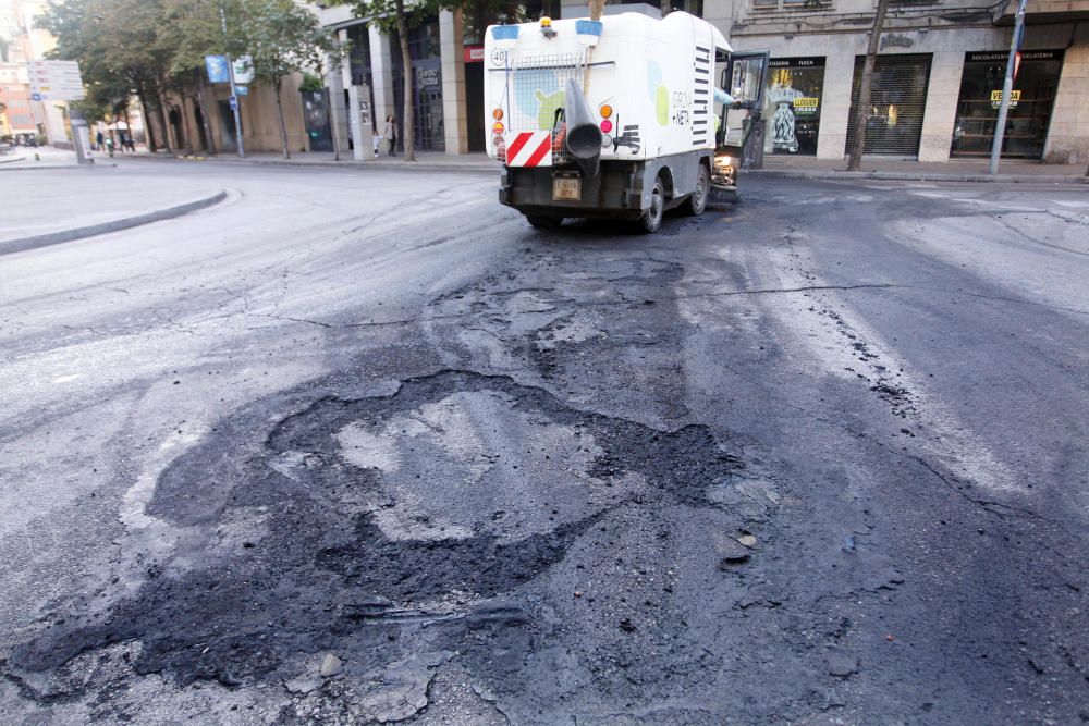 Carrers amb restes de mobiliari urbà cremat, contenidors per terra i treballadors de la brigada treballant