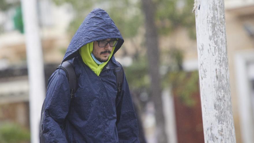 Un chico se aguarda de la lluvia con un chubasquero.