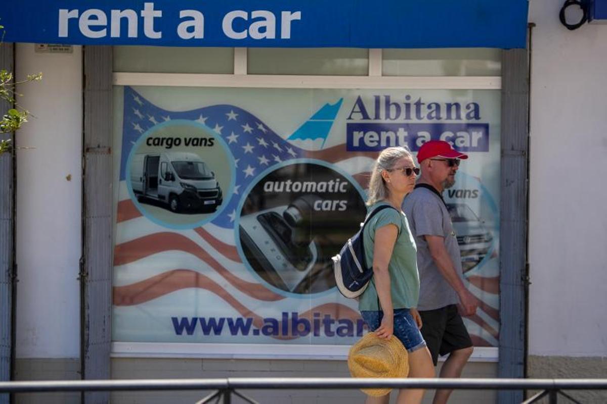 Una pareja pasa por delante de una oficina de alquiler de coches con el escaparate decorado con motivos estadounidenses próxima a la Base Naval en Rota.