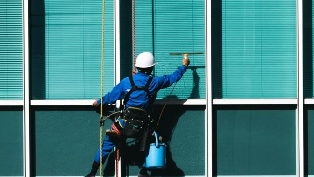 Un trabajador limpia las ventanas de un edificio, persianas incluidas