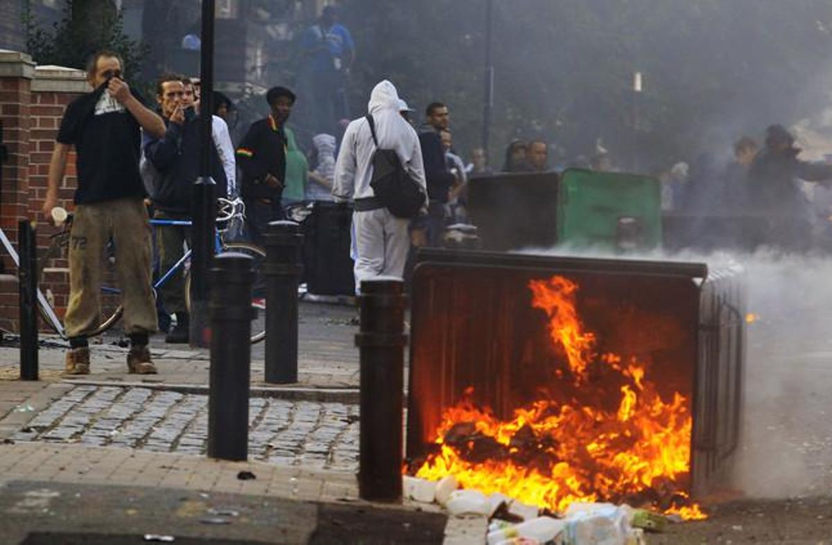 Veïns de Hackney, a l’est de Londres, es parapeten darrere un contenidor en flames durant els disturbis (Anglaterra).