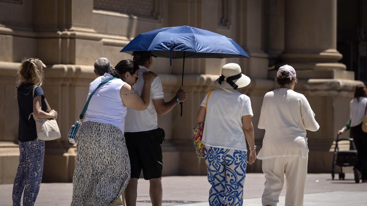 Varias personas se protegen del calor con un paraguas en la plaza del Pilar de Zaragoza