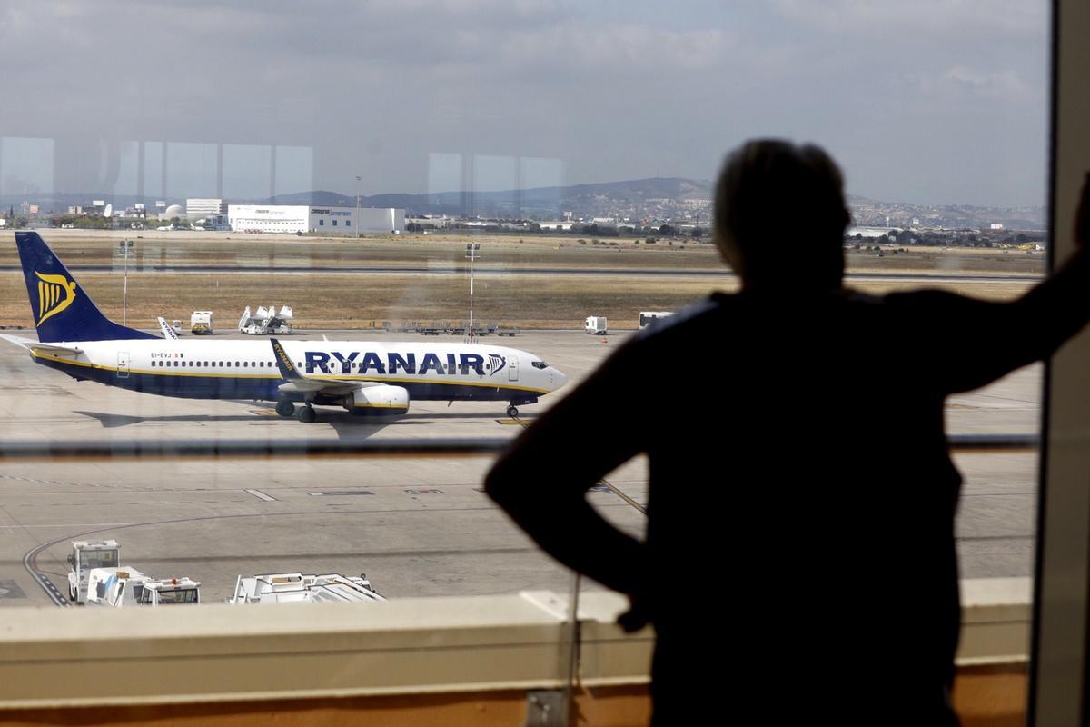 Un pasajero mira por la cristalera con un avión de Ryanair de fondo, en el aeropuerto de Valencia.