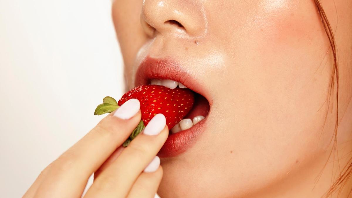 Una mujer comiendo una fresa.