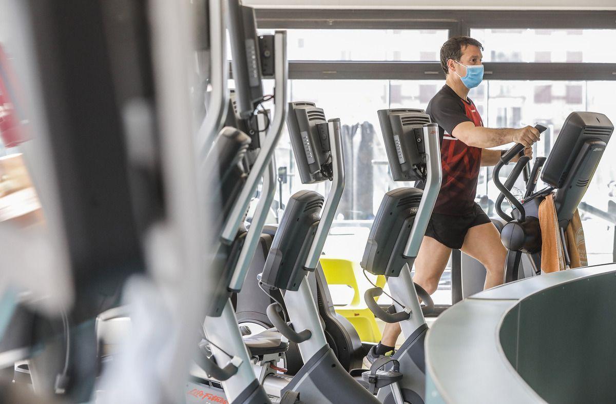 Un hombre con mascarilla utiliza las máquinas de un gimnasio.