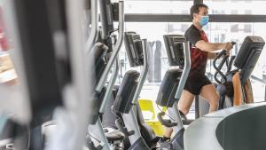 Un hombre con mascarilla utiliza las máquinas de un gimnasio.