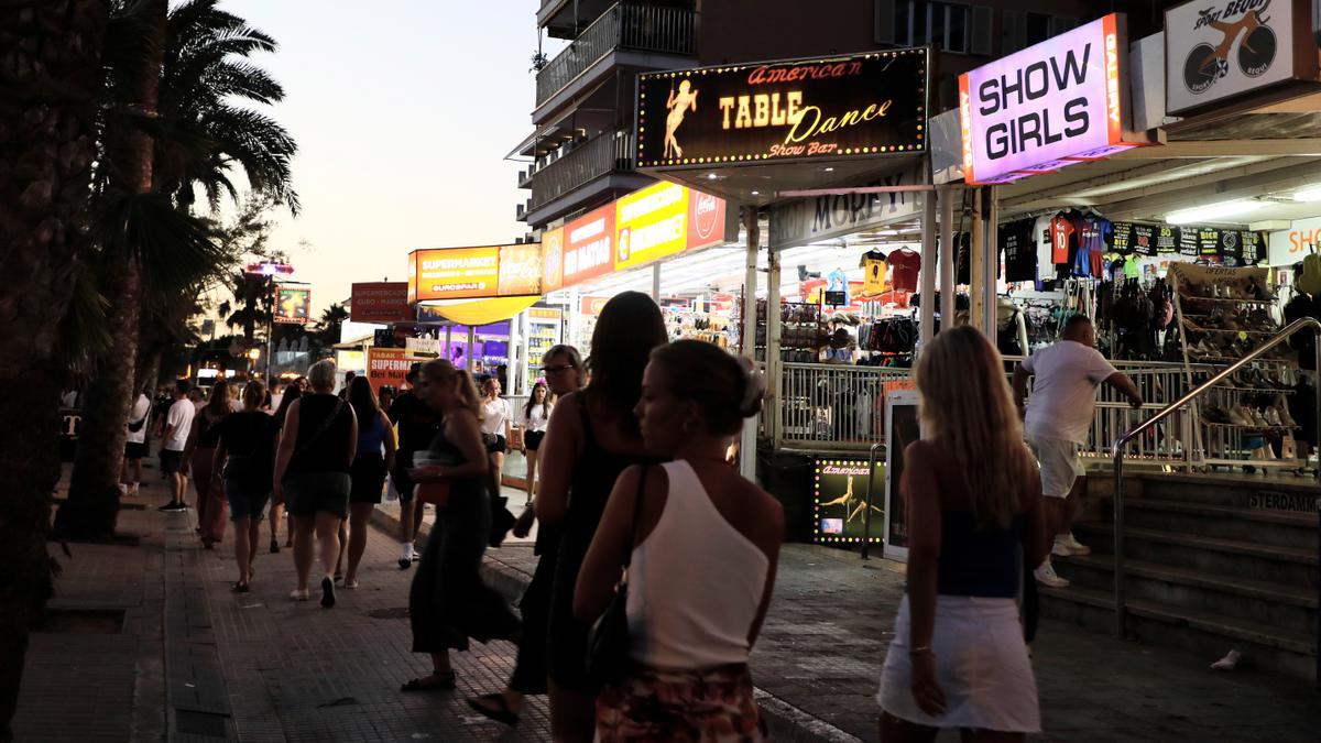 Menschen spazieren auf der Strandpromenade von Arenal auf Mallorca an Show-Bars vorbei.