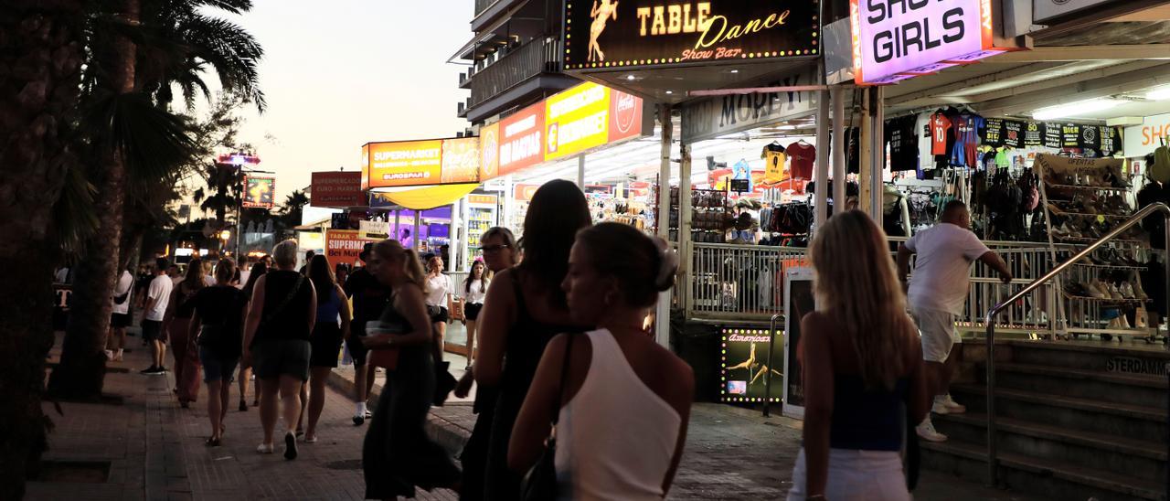 Menschen spazieren auf der Strandpromenade von Arenal auf Mallorca an Show-Bars vorbei.