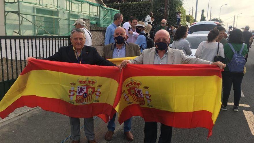 Tres hombres esperan a Juan Carlos I en Sanxenxo con banderas de España.