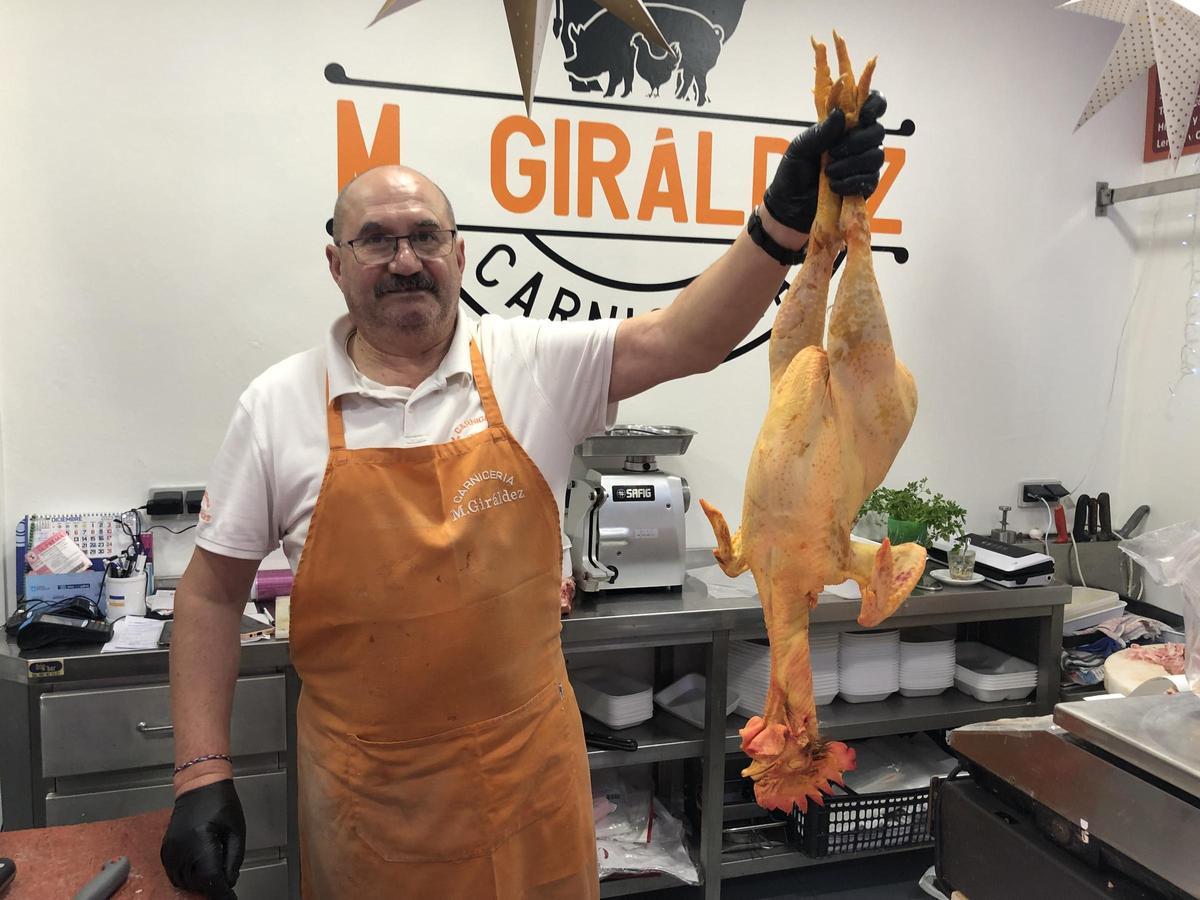 Marcial Giráldez en su carnicería con un gallo de corral