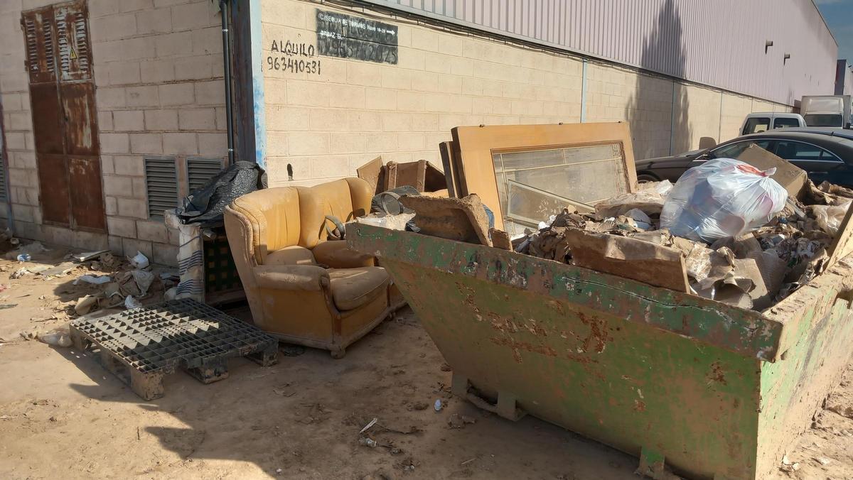 Sofás y otros enseres esperan a ser retirados junto a un contenedor de obras.