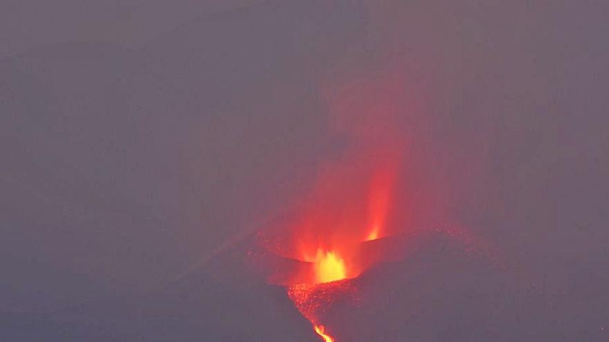  Vista general del volcán de Cumbre Vieja, en el que son visibles dos bocas abiertas y una colada de lava que desciende por el lado de un cono volcánico. llano.