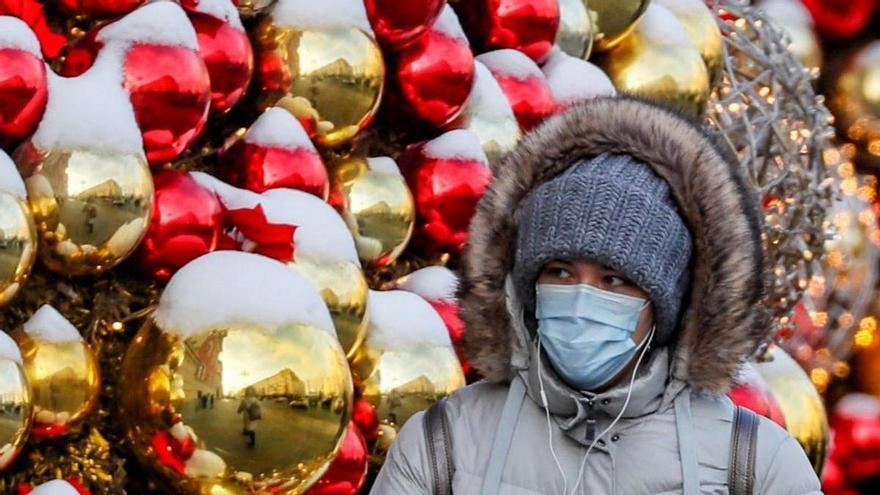 Una mujer camina protegida con una mascarilla por una calle con adornos navideños.