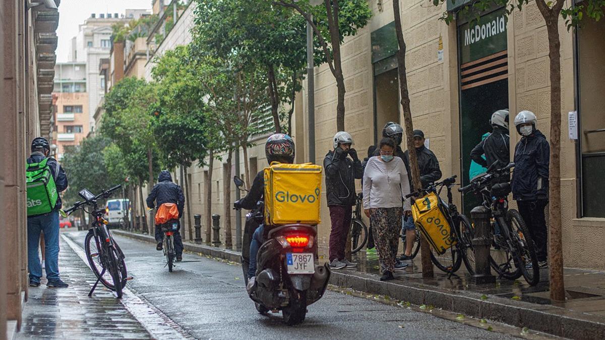 Un grupo de 'riders' esperan para recoger pedidos ante un establecimiento de comida rápida de Gràcia, el 14 de mayo