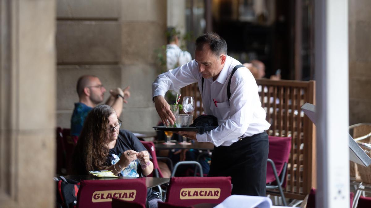 Un camarero atiende a un cliente en la terraza de un bar.