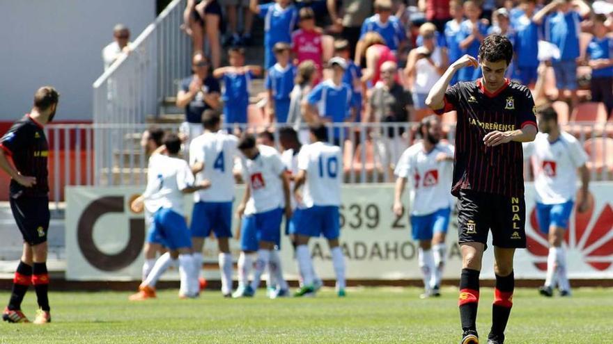 Dos jugadores del Condal, cabizbajos, mientras al fondo los futbolistas del Rayo Majadahonda celebran un gol.