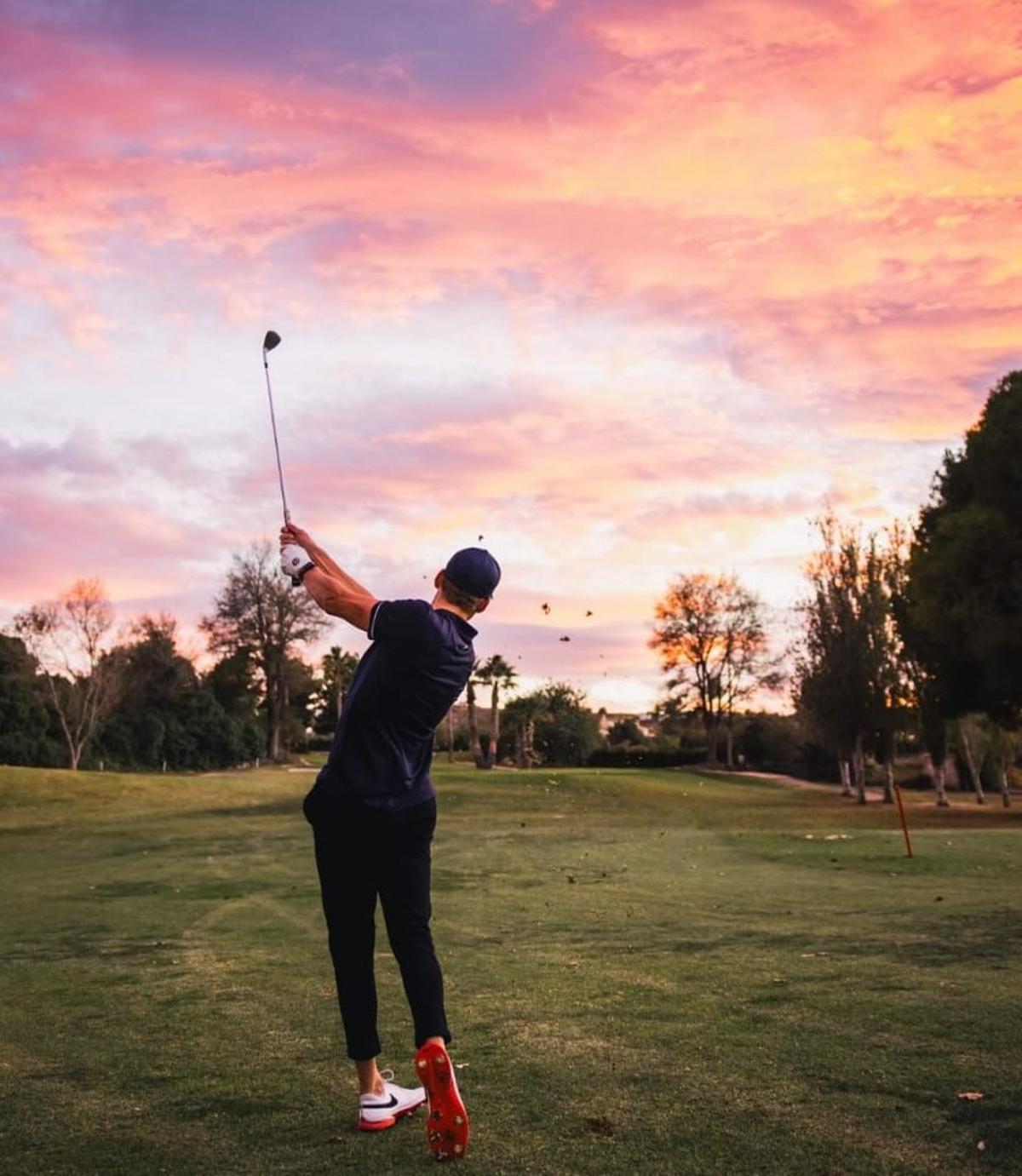 El ciclista practica sus golpes de golf bajo el cielo anaranjado de los atardeceres de otoño