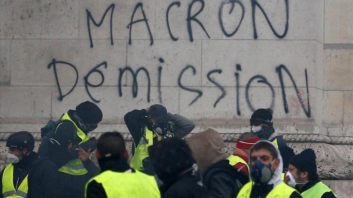 Manifestantes de los 'chalecos amarillos' ante una pintada que pide la dimisión de Macron, en París.