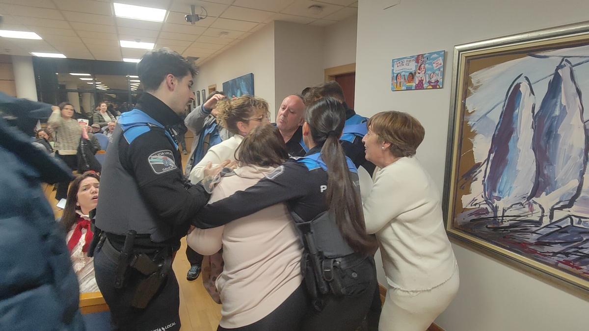 Estela Santomé es acompañada por los agentes fuera del salón de plenos en medio de un tumulto.