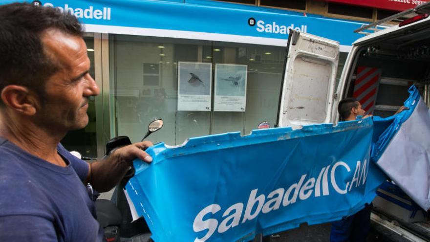 Unos operarios sustituyen la cartelería de una oficina del Sabadell.