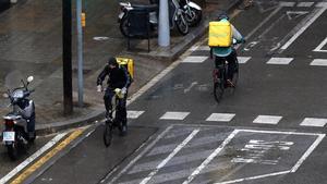 Dos ’riders’ de Glovo, circulando bajo la lluvia por la calle de Provença, el pasado 16 de marzo.