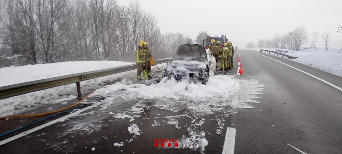 Els Bombers treballant en l'incendi del cotxe accidentat i cremat