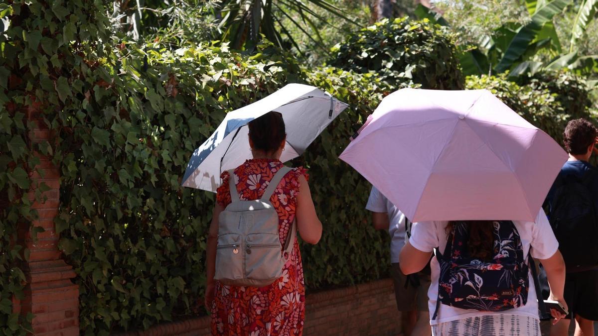Varias personas se refugian del sol con paraguas.