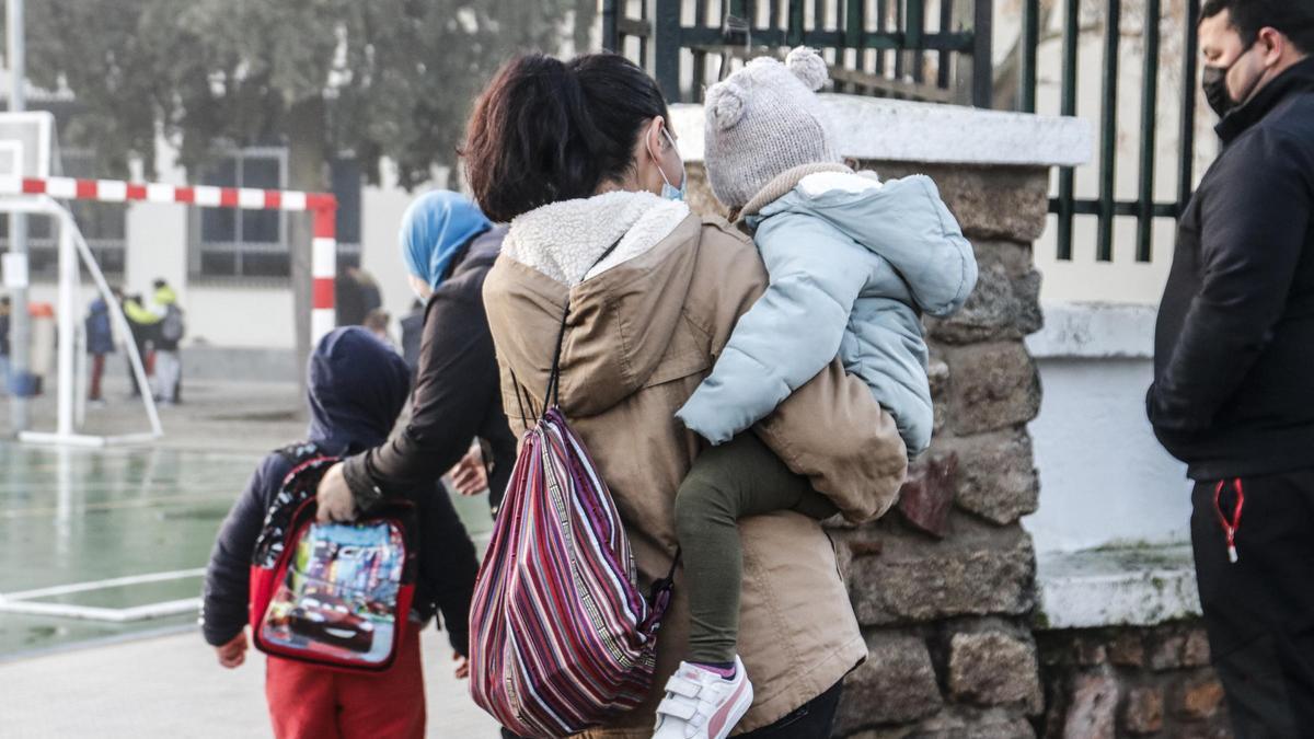 Una mujer sostiene en brazos a un niño en la puerta de un colegio en Cáceres.