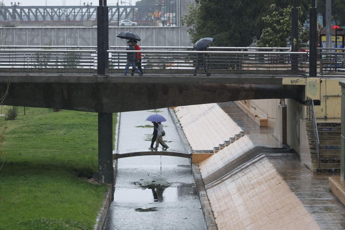 Varias personas se protegen de la lluvia con un paraguas este miércoles sobre el cauce del Guadalmedina de Málaga.