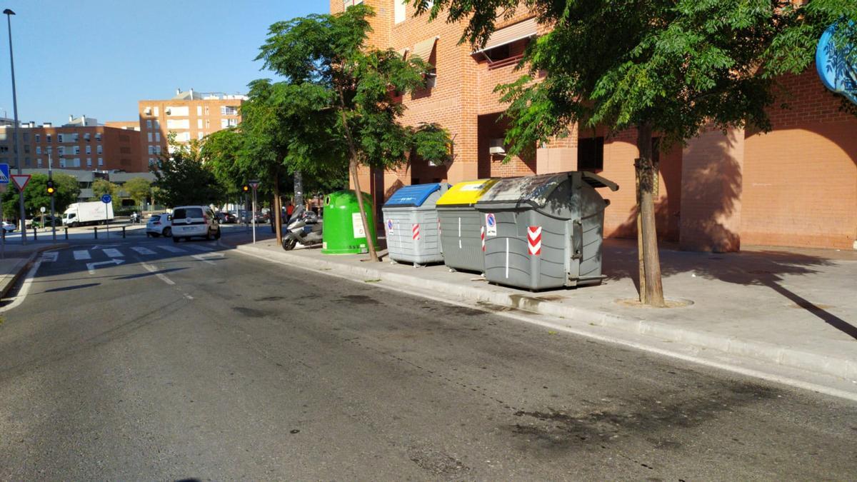 El poste, negro al estar cubierto aún por bolsas, queda oculto entre los contenedores y los árboles, al lado del que reciclaje de vidrio