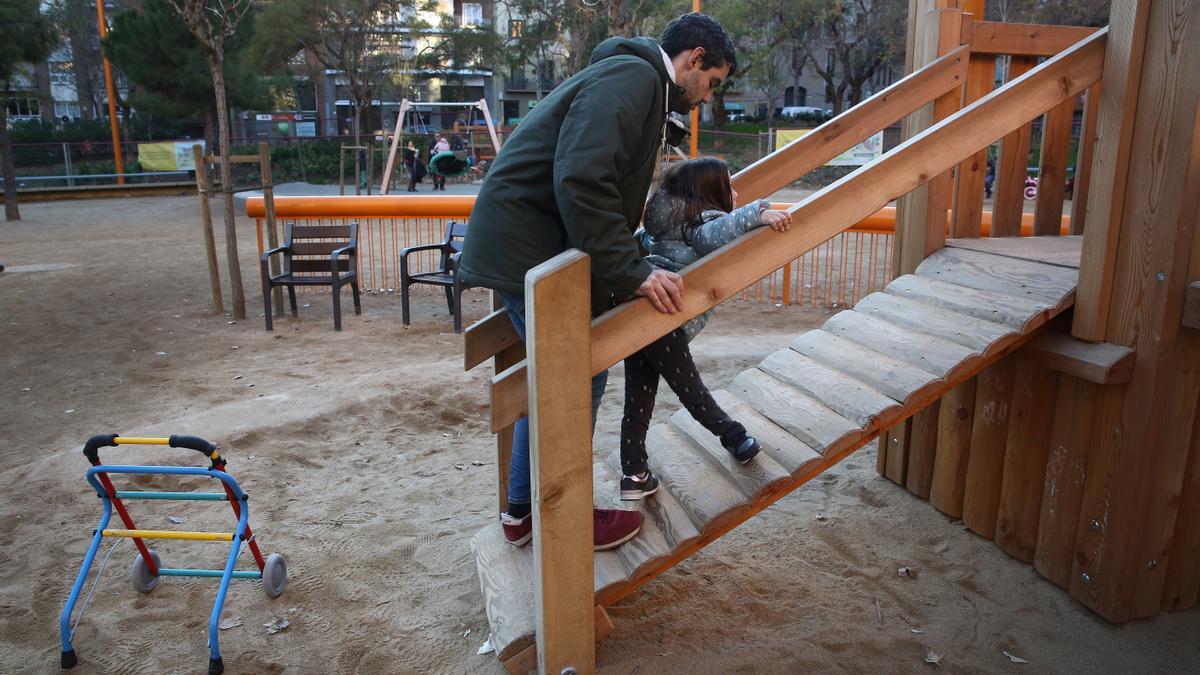Un padre ayuda a su hija a acceder a un juego en los Jardines de la Industria de Barcelona.