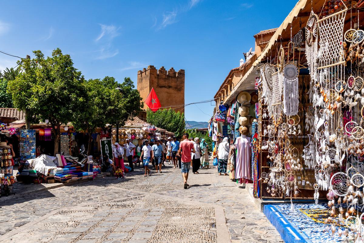 Vibrante escena callejera en Chefchaouen con coloridos puestos de mercado, artículos hechos a mano y una torre histórica en el fondo.