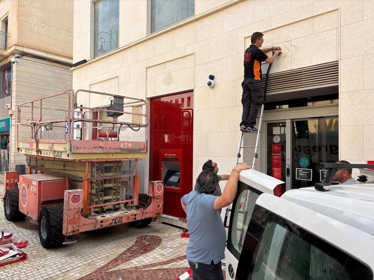 Varios operarios quitan los últimos carteles del Banco Santander en la Plaça de Baix de Elche