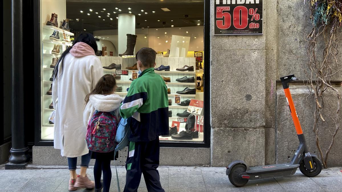 Varias personas en el escaparate de un comercio que anuncia descuentos del 50% por el Black Friday