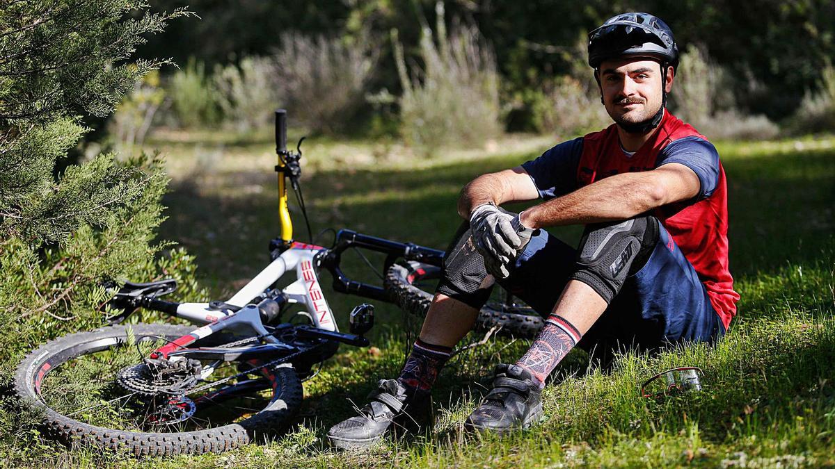 El ‘rider’ de Sant Joan posa sentado, ataviado con casco y protecciones, junto a su bicicleta de montaña. | T. ESCOBAR