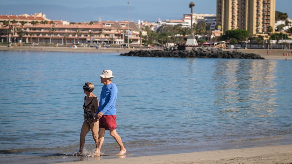 Una pareja de turistas pasea por la orilla de una playa del sur de Tenerife.
