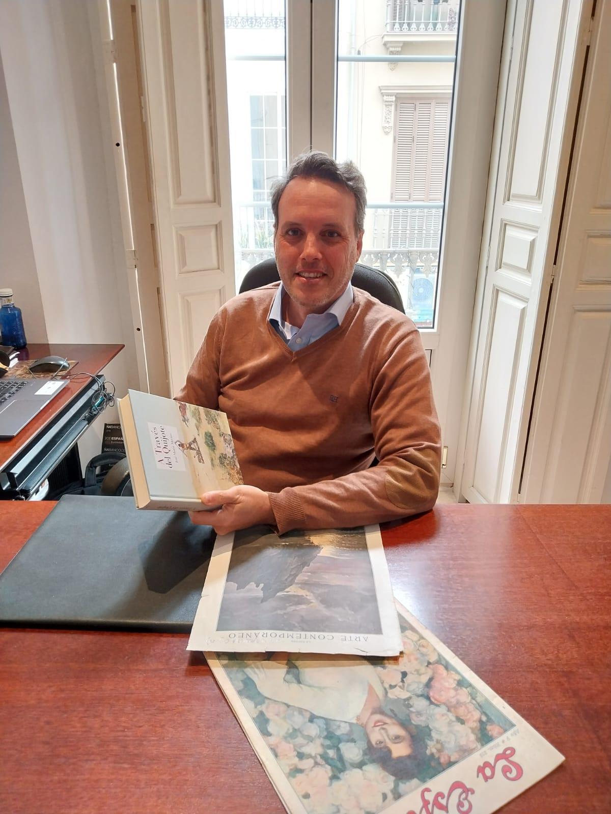 Antonio Castillo, en su despacho, con la portada de un libro del académico de la Lengua José María Merino que reproduce uno de sus cuadros.