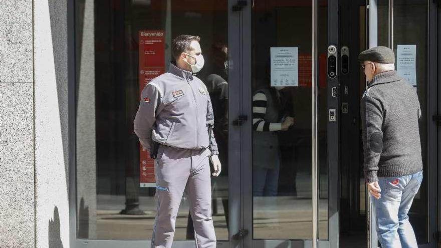 A la derecha, un jubilado entra en una sucursal bancaria de Avilés en presencia de un guardia de seguridad de la entidad.