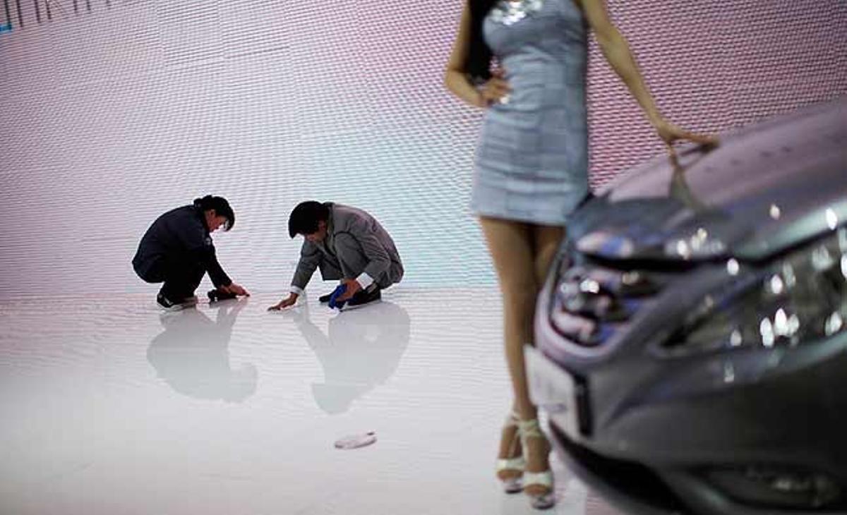 Empleats netegen el terra mentre una model es fotografia al costat d’un vehicle durant la 14a Exhibició Internacional de la Indústria de l’Automòbil de Xangai (Xina).